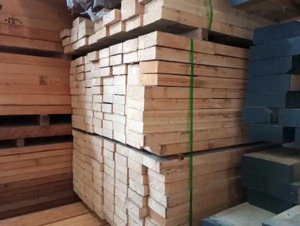 Piles of light-colored lumber, possibly madera ayous, are stacked high. A stack of dark wood is visible on the right.