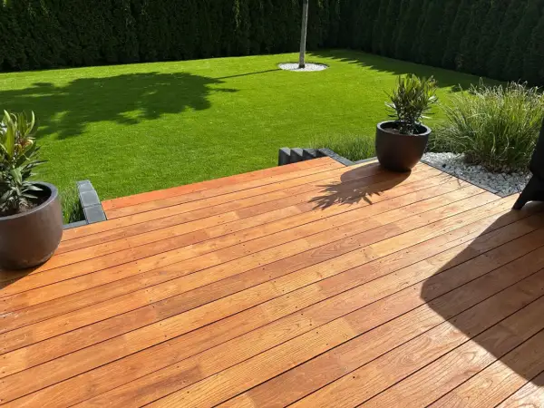 Terraza de madera de robinia con césped verde y plantas en macetas.
