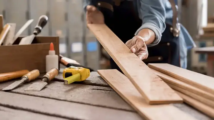 Carpintero examinando tablas de madera, listo para aprender como quitar pintura de la madera. Herramientas de carpintería a la vista.